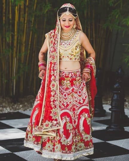 Red Punjabi bridal lehenga with heavy embroidery and embellished golden <em>choli</em>
